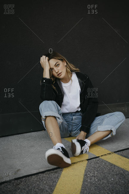 Young woman with head in hands sitting on footpath against wall