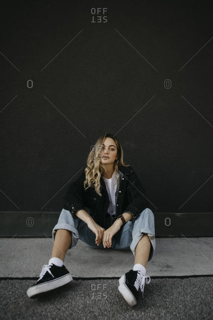 Woman sitting on footpath against wall