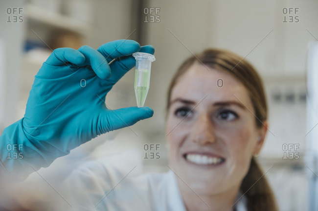 Smiling woman looking at test tube while holding in hands at laboratory