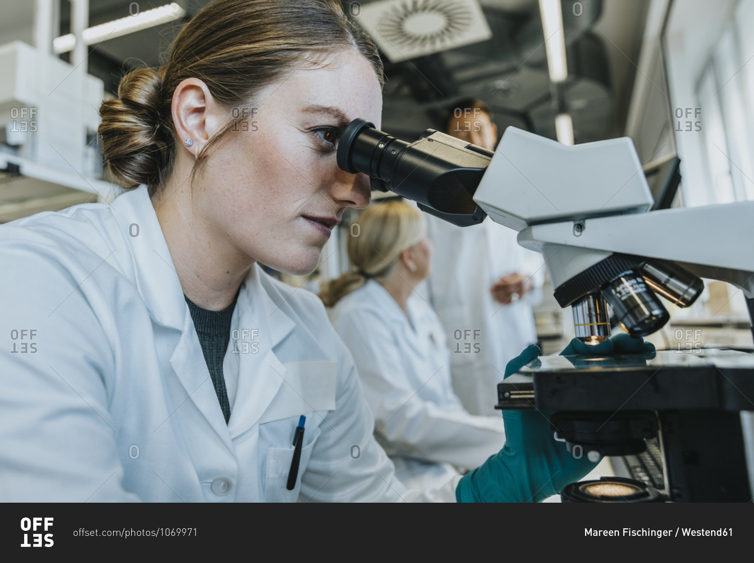 Assistant analyzing human brain microscope slide while sitting with scientist in background at laboratory