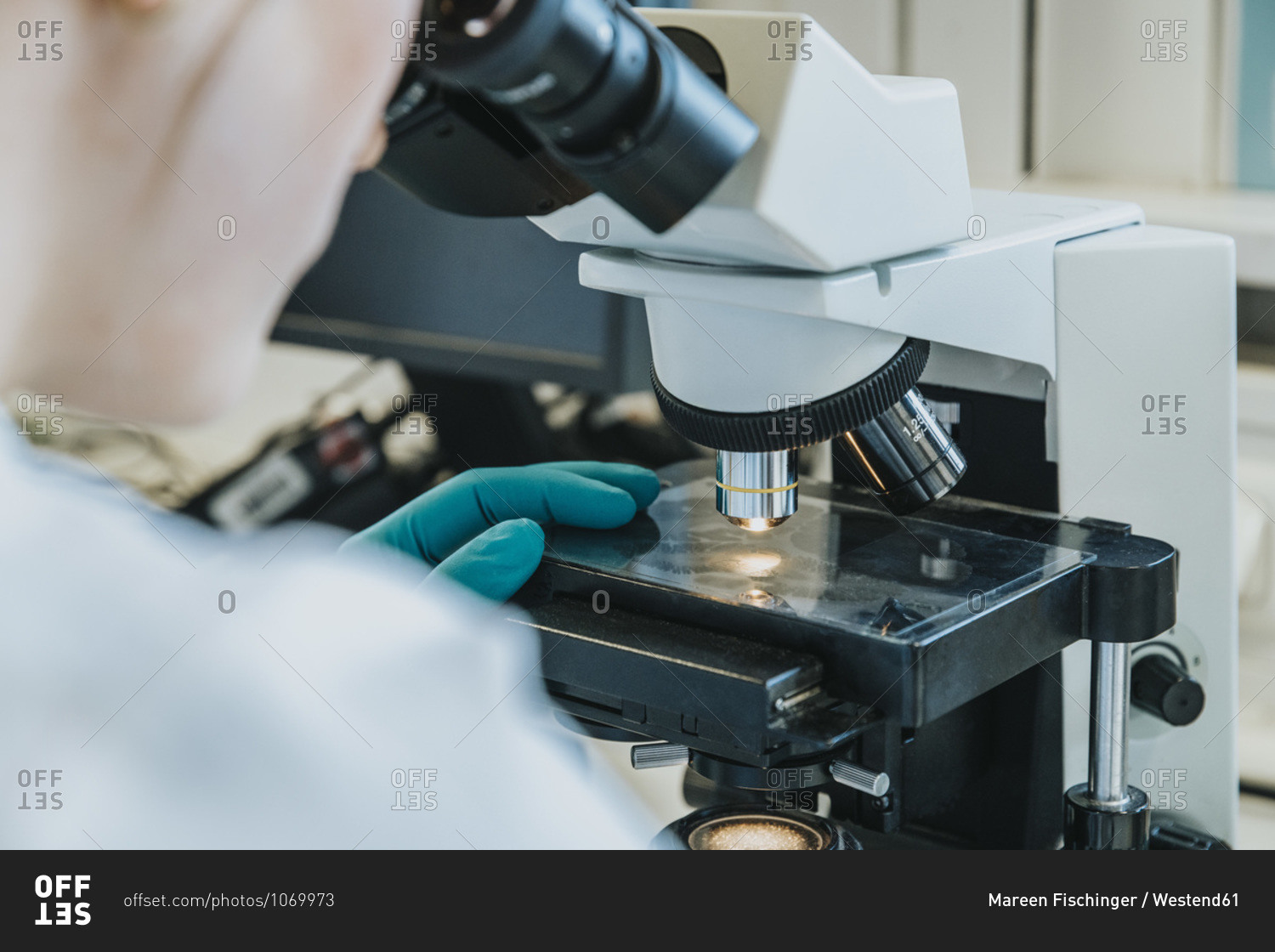 Young woman analyzing human brain microscope slide under microscope while sitting at laboratory