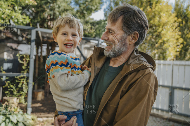 Father laughing while carrying son standing in back yard on sunny day