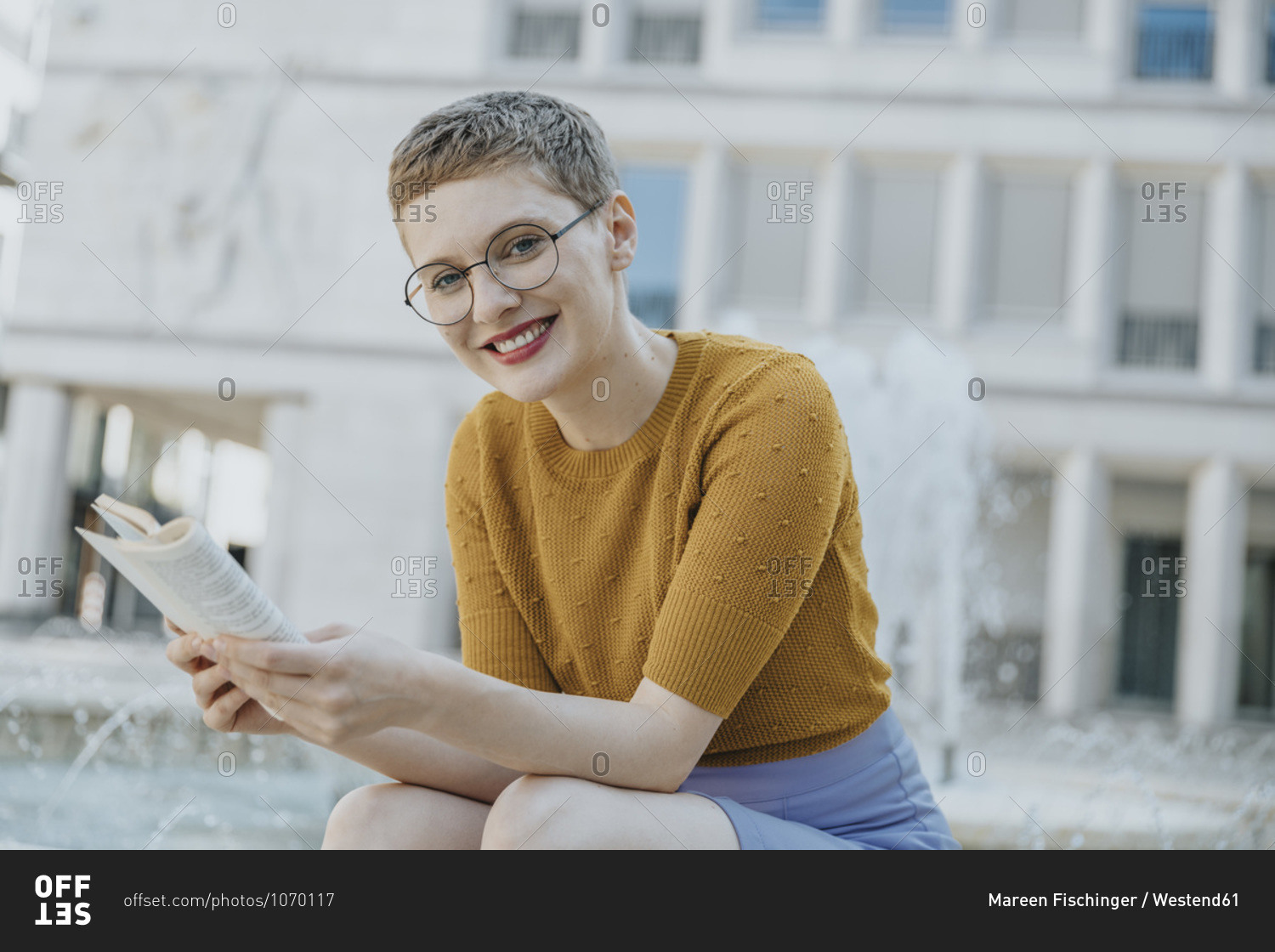 Smiling mid adult woman with book sitting against fountain