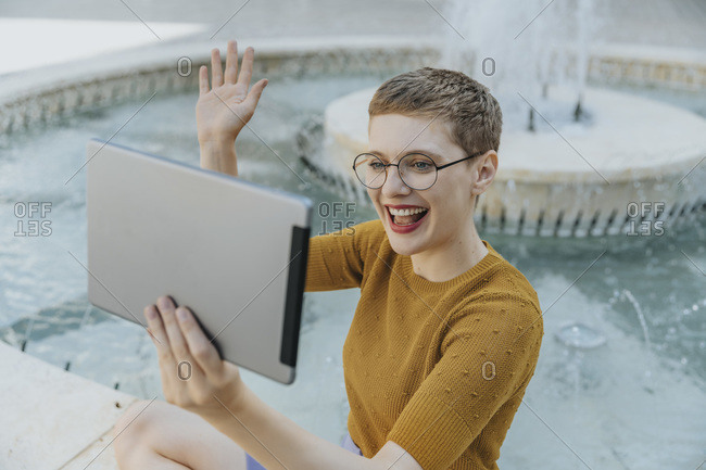 Woman doing video call with digital tablet sitting by fountain on sunny day