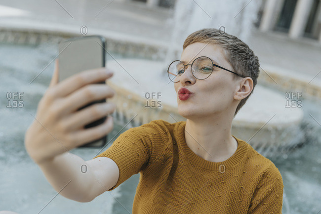 Mid adult woman taking selfie on smart phone standing against fountain