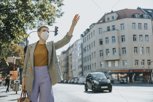 Woman wearing protective face mask calling taxi by waving standing on street in city