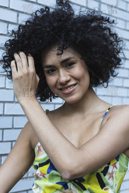 Smiling young woman with hand in hair standing against tiled wall
