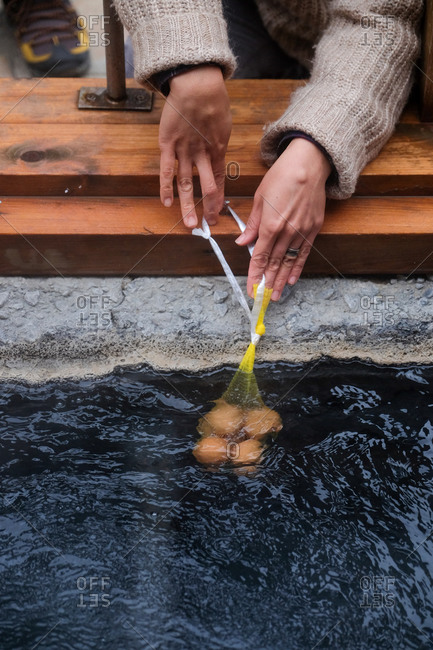 Hands holding eggs in the hot waters of onsen in Japan to make onsen tamago traditional Japanese low temperature eggs