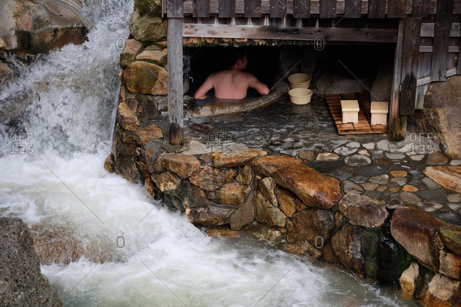 Wakayama, Japan - November 18, 2017: Water rushing in river beside building enclosing a natural Japanese onsen hot spring with man bathing inside