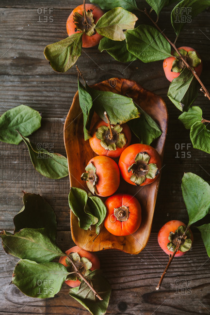 Persimmons on a wooden dish on rustic table with leaves