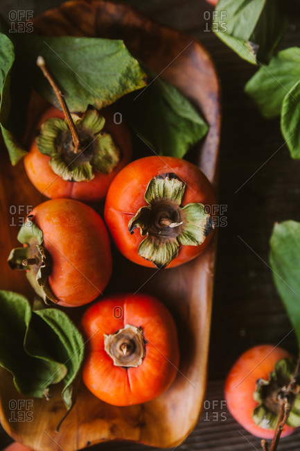 Close up of persimmons on a wooden dish on rustic table with leaves