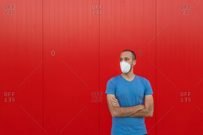 Young man wearing respiratory mask while looking away near colorful red wall during coronavirus pandemic