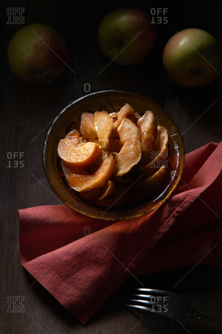 From above of bowl with delicious sweet sliced baked apples served on table with fork and napkin