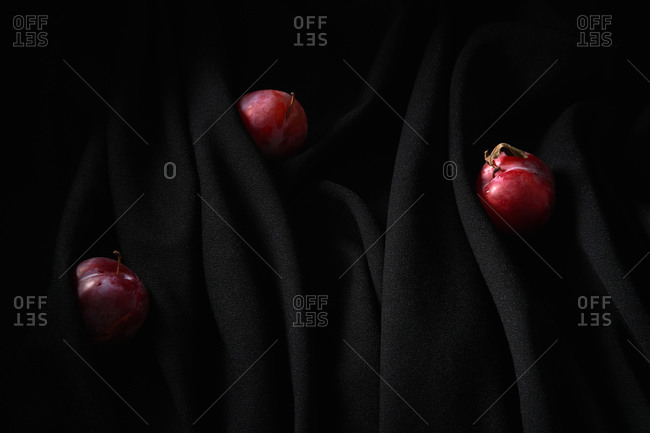 Red small cherries on thin stems placed on dark black wrinkled cloth in studio