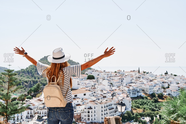 Back view of anonymous female traveler standing on terrace at viewpoint and admiring spectacular cityscape of Frigiliana on sunny day in summer