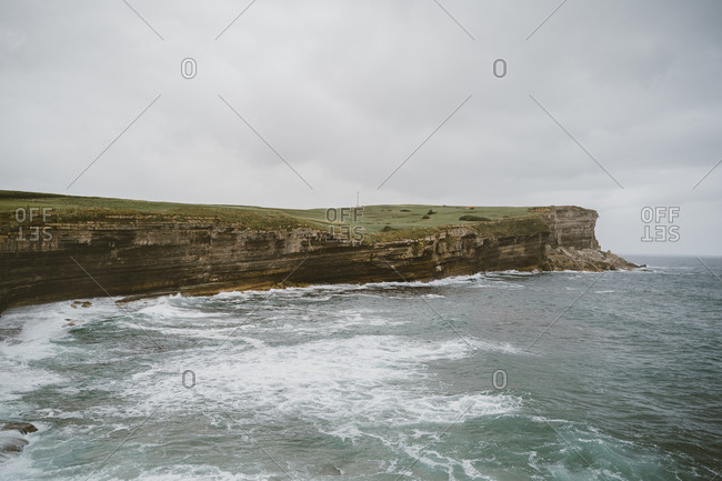Scenic landscape of rocky cliff near stormy sea under gray sky in overcast weather
