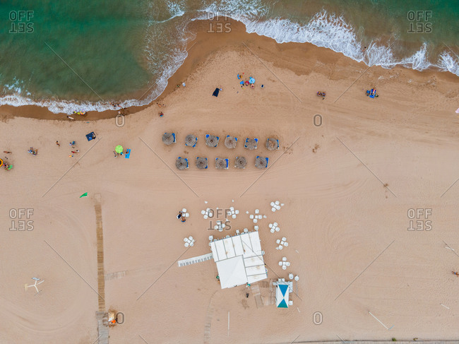 Magnificent aerial view of turquoise sea waving on sandy coastline with deckchairs and umbrellas in summer