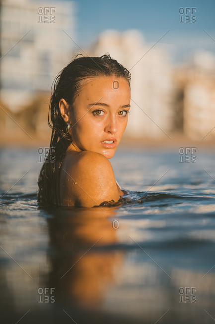 Charming female in sea water while looking at camera at sunset during vacation in summer