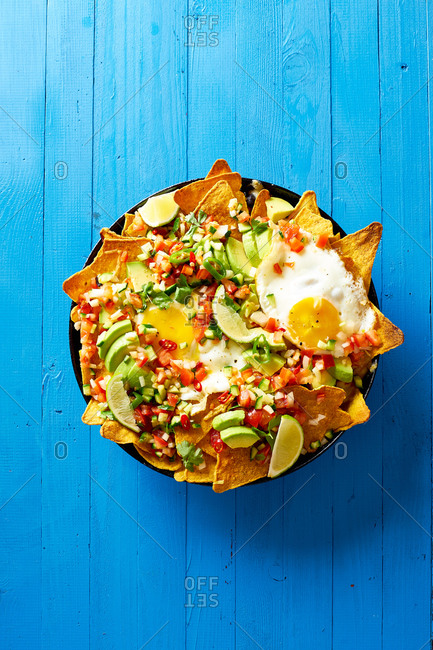 Chilaquiles - Mexican breakfast made of black beans, corn, tortilla chips and fried eggs on blue wooden table