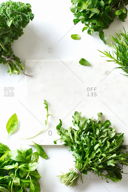 Flat lay with various herbs and lettuce and marble cutting board on white background
