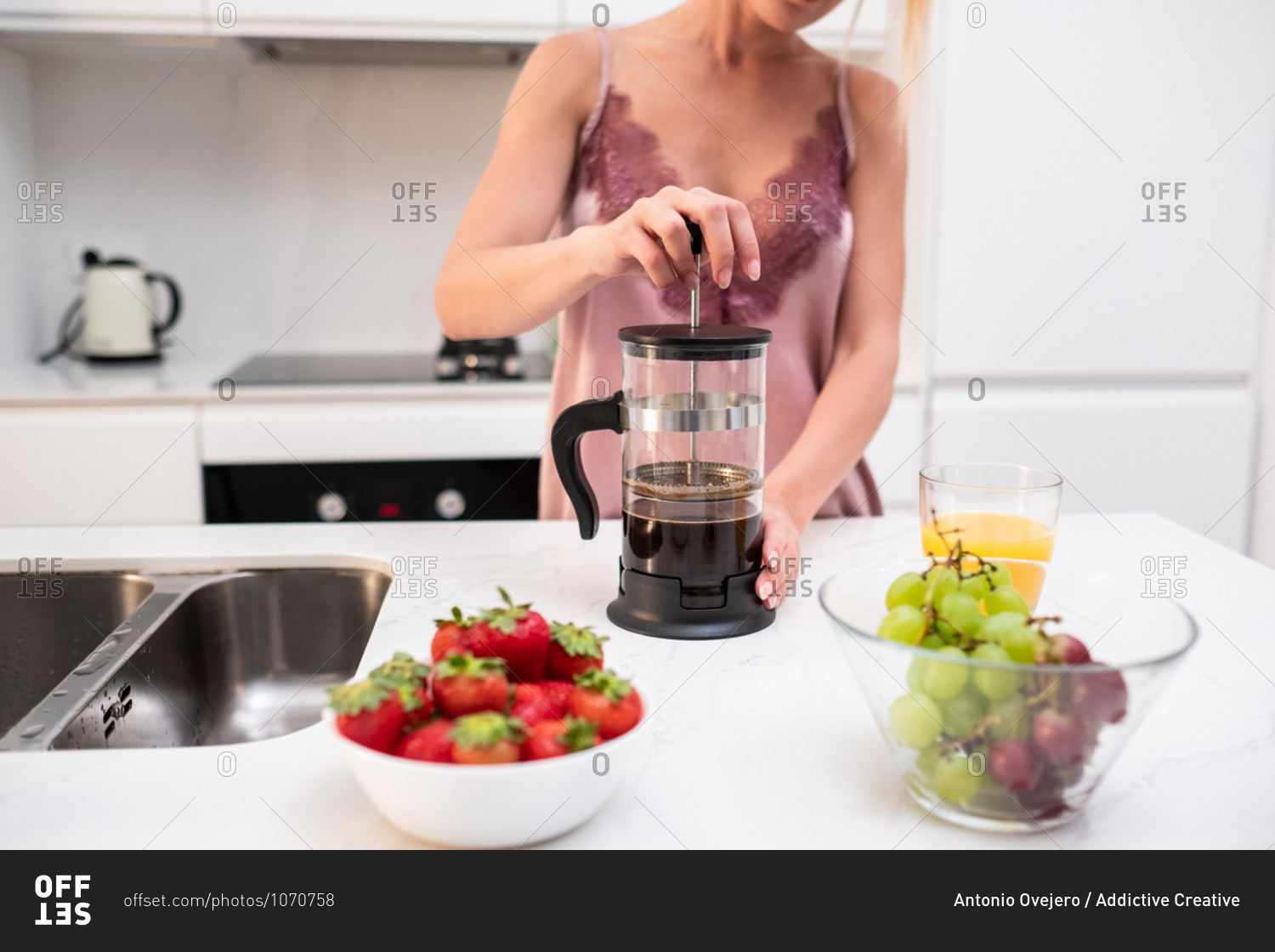 Unrecognizable female in silk pajama standing at counter in kitchen and preparing aromatic coffee in French press