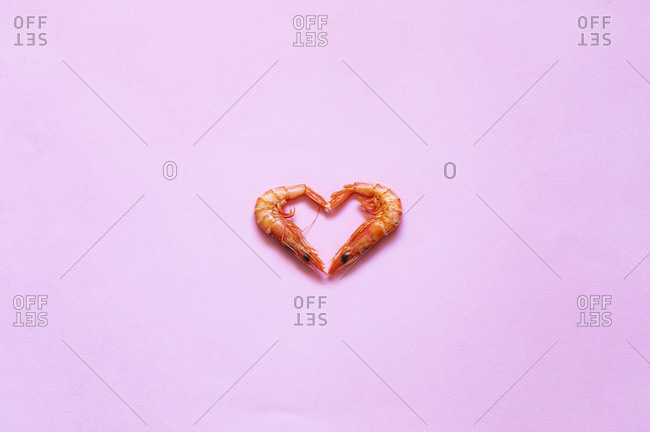 Raw prawns placed in shape of heart on bright pink background in studio