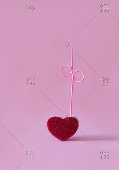 Red vivid heart with curved straw placed on pink background in modern studio