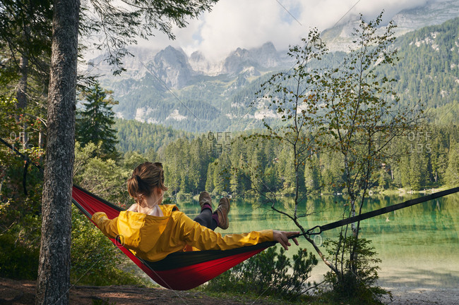 Back view full length of unrecognizable traveler relaxing in hammock and enjoying landscape of Dolomites mountains and lake