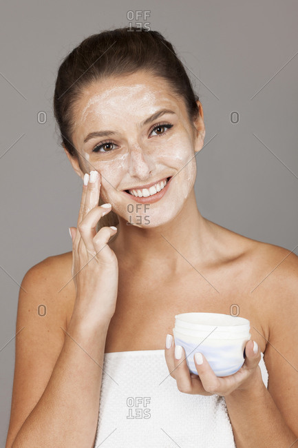 Content woman using nourishing cream from pot on hand and looking at camera isolated on gray background