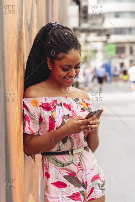 Content ethnic female in trendy outfit text messaging on cellphone on pavement in town