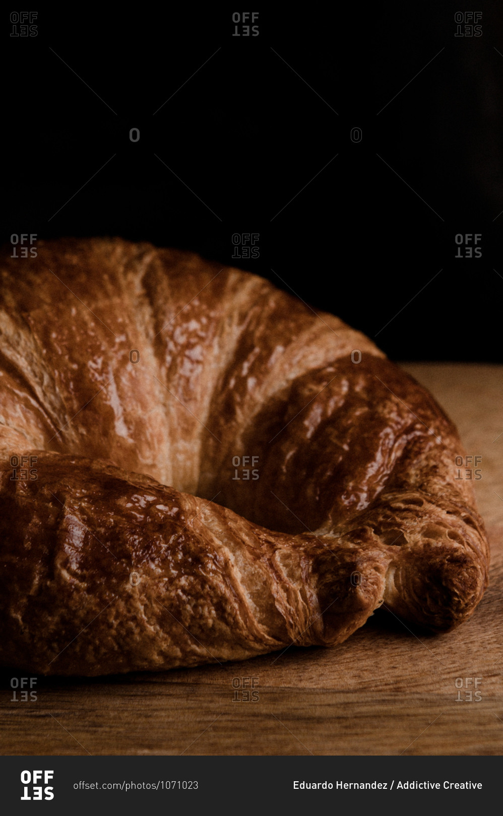 Closeup of appetizing crispy croissant placed on wooden table against black background