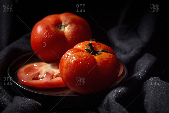 Fresh ripe red grape tomatoes with water drops in metal bowl placed on table dark background