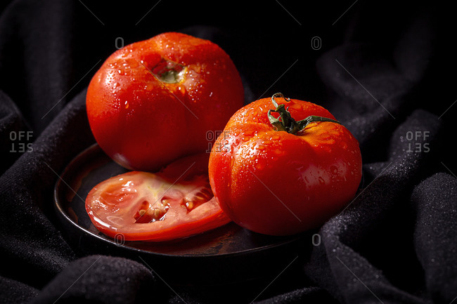 Fresh ripe red grape tomatoes with water drops in metal bowl placed on table dark background
