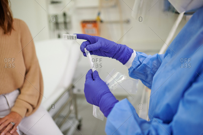 From above of crop unrecognizable doctor in uniform with vaccine tube near female patient in hospital