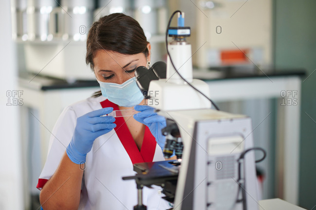 Female specialist in uniform with medical sample near microscope at work in laboratory