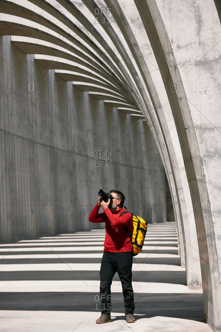 Traveling male photographer with professional photo camera taking picture of amazing arched passage in city on sunny day