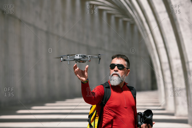 Elderly male photographer standing in archway on sunny day with modern flying drone in La Palma