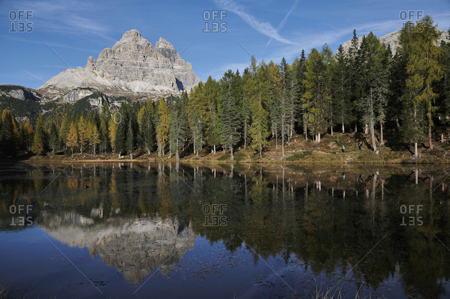 Amazing landscape of lake with calm water located near evergreen woods on sunny day on background of the Dolomites mountain range in Italy