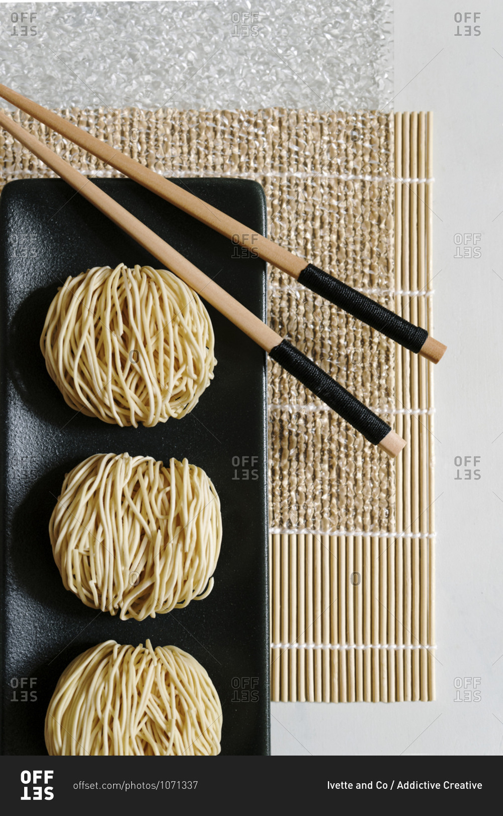 From above of round Asian noodles and wooden chopsticks arranged on bamboo mat on table in cafe