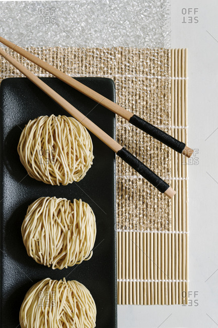 From above of round Asian noodles and wooden chopsticks arranged on bamboo mat on table in cafe