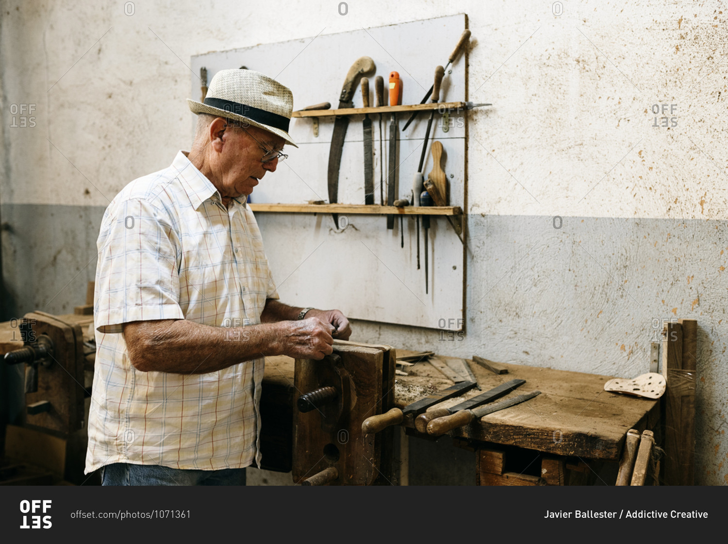 Side view of senior male carpenter grinding wooden details while making handmade folding fans in messy workshop