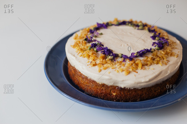 Appetizing rustic homemade cake topped with white cream and decorated with nuts and edible flowers served on plate on white table