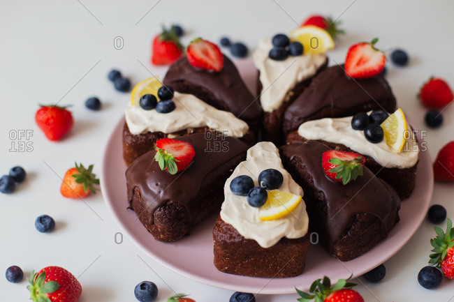 Closeup delectable homemade chocolate cake with white and chocolate cream decorated with fresh berries and lemon slices and cut into pieces