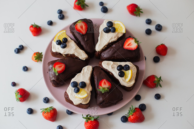 Delectable homemade chocolate cake with white and chocolate cream decorated with fresh berries and lemon slices and cut into pieces