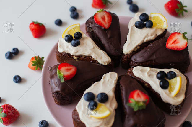 Closeup delectable homemade chocolate cake with white and chocolate cream decorated with fresh berries and lemon slices and cut into pieces