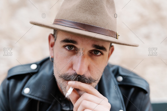 Cool handsome guy in with gorgeous mustache smoking cigarettes and looking at camera on blurred background