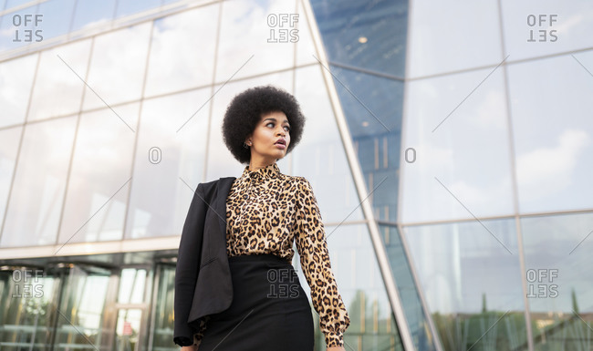 From below of confident African American female in formal wear standing near modern office building in downtown