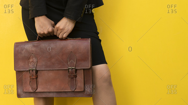 Crop anonymous female in skirt with stylish brown leather handbag standing against yellow background