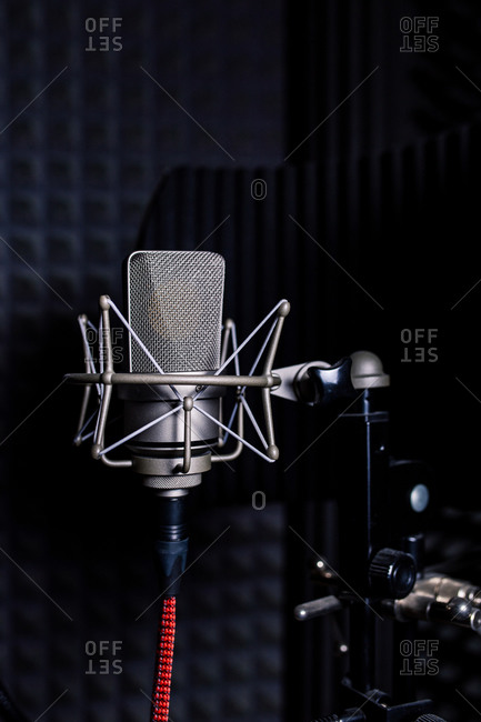 Contemporary metal microphone with wire placed on background of soundproof foam with pyramid shaped pattern in dark music recording studio