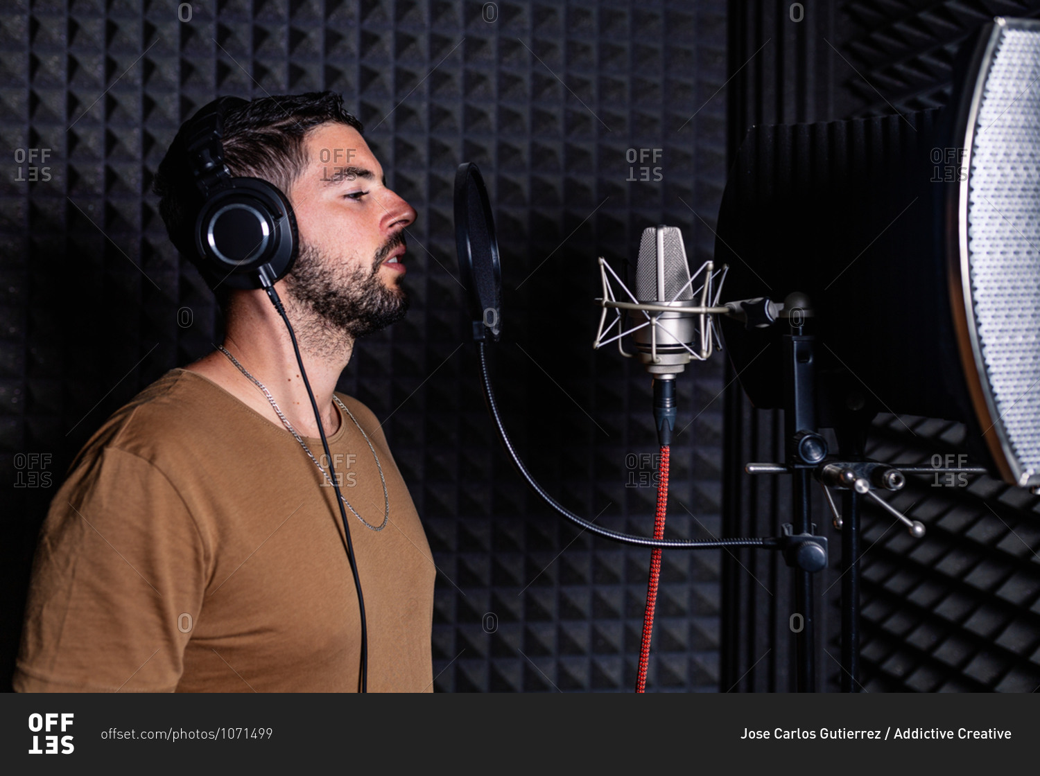 Side view of male singer in headphones standing in acoustic room with soundproof walls and microphone and recording song in studio